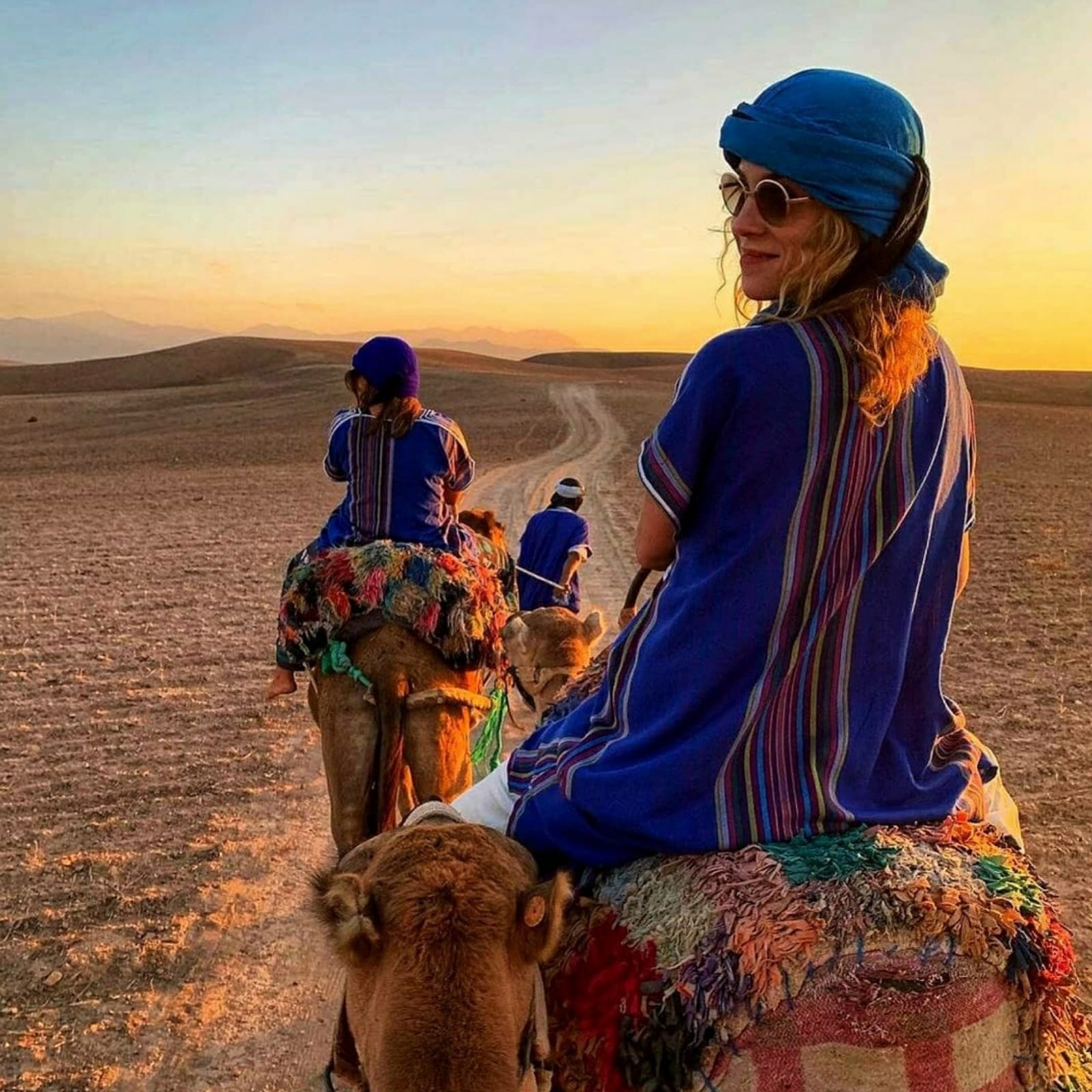 Traveller in a blue Berber tunic looking back from an Agafay sunset camel ride near Marrakech