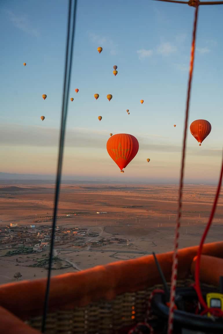 Hot-air balloons in the sky above a village and plain at sunrise, seen from a balloon basket