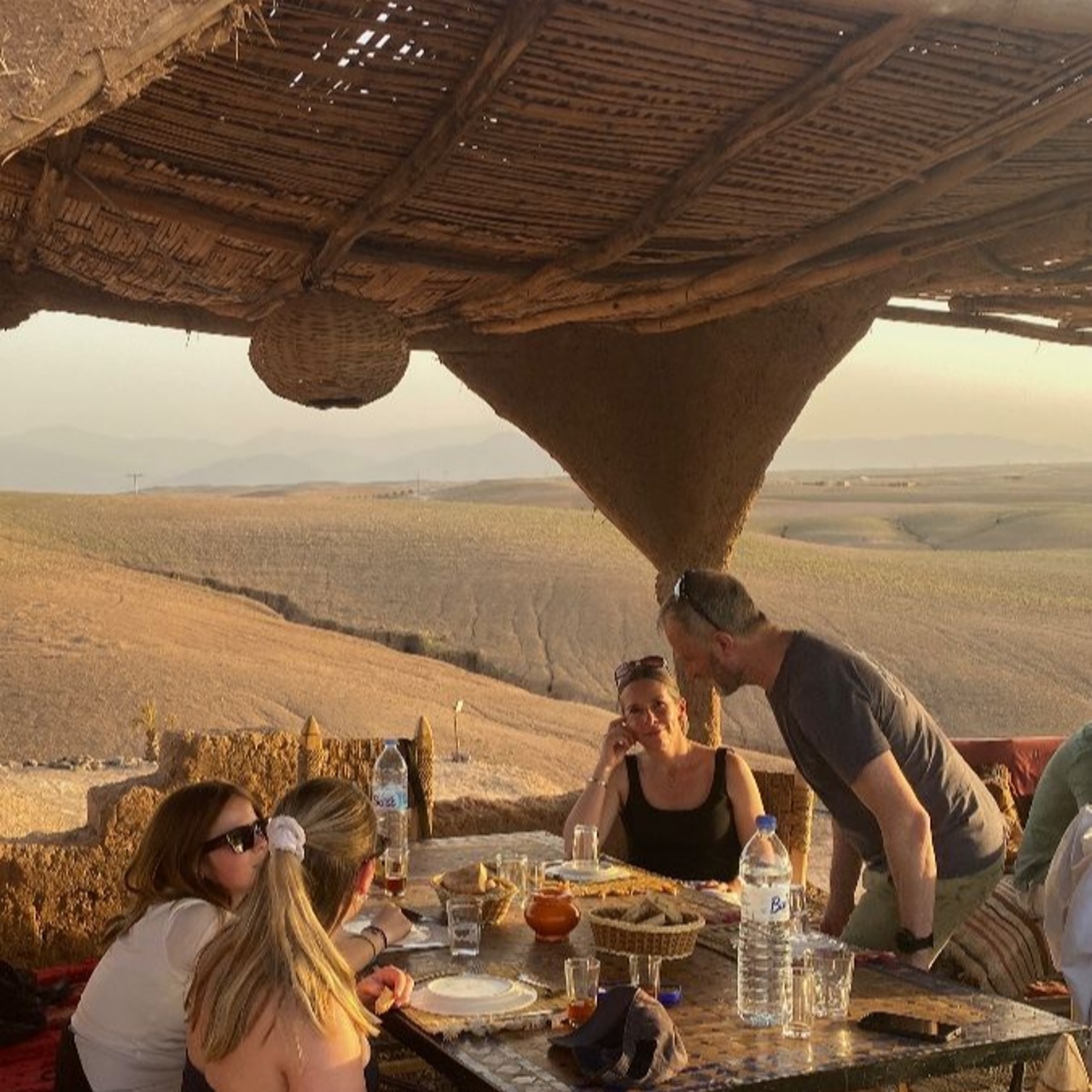 Guests sharing a Moroccan meal on a shaded desert terrace overlooking the Agafay valley
