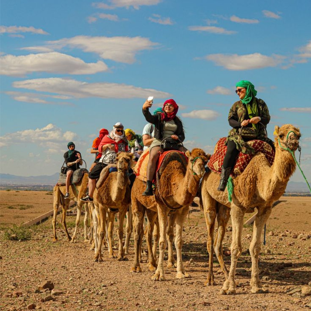 Group enjoying an Agafay camel ride from Marrakech along a stony desert track under a blue sky